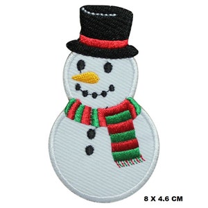 Könnte beinhalten: Weißer Schneemann mit einem schwarzen Zylinder, einem rot-grünen gestreiften Schal und schwarzen Augen und Knöpfen. Der Schneemann ist 8 x 4,6 cm groß.