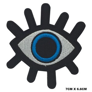 May include: Black and white embroidered eye patch with a blue circle in the center. The eye patch is 7 cm by 6.6 cm.