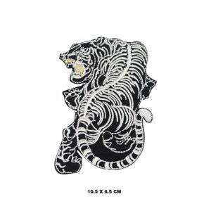 Op de afbeelding: Zwarte geborduurde strijkpatch met een witte skelettige tijger met gouden accenten. De patch is 10,5 cm bij 6,5 cm.