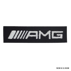 Op de afbeelding: Zwarte geborduurde patch met witte "AMG" belettering en drie witte strepen. De patch is 9 cm bij 2,5 cm.