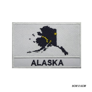 May include: White embroidered patch with a blue outline of the state of Alaska and a yellow star. The text "ALASKA" is written in white below the outline.
