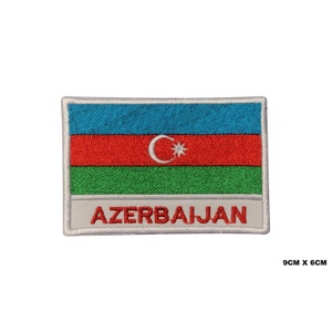 May include: Embroidered patch featuring the flag of Azerbaijan. The flag is blue, red, and green with a white crescent moon and star in the center. The patch is 9 cm by 6 cm and has the word "AZERBAIJAN" written below the flag.
