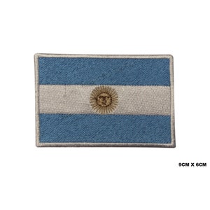 Op de afbeelding: Een geborduurde patch van de Argentijnse vlag. De vlag is blauw en wit met een gouden zon in het midden. De patch is 9 cm bij 6 cm.