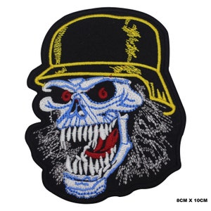 Könnte beinhalten: Gestickter Aufnäher mit einem Totenkopf, der einen schwarzen Hut mit gelbem Rand trägt. Der Totenkopf hat rote Augen, blaue Akzente und eine rote Zunge. Der Aufnäher misst 8 cm x 10 cm.