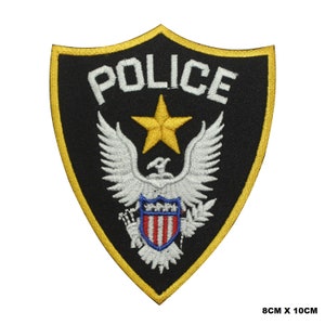 May include: A black and gold embroidered patch with the word "POLICE" in white lettering. The patch features a white eagle with a red, white, and blue shield and a gold star.