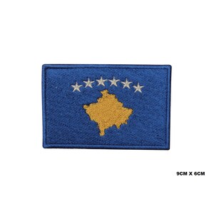 May include: Embroidered patch of the Kosovo flag. The flag is blue with a gold outline of the country's shape and six white stars in a semi-circle at the top. The patch measures 9 cm by 6 cm.