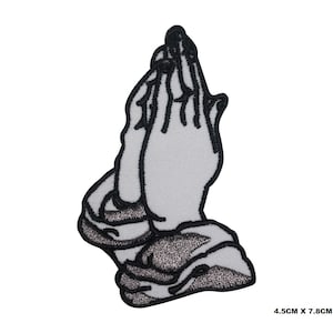 May include: Black and white embroidered patch of two hands clasped in prayer. The patch is 4.5 cm by 7.8 cm.