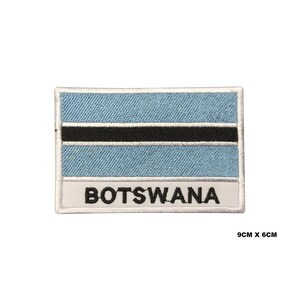 May include: An embroidered patch featuring the flag of Botswana. The patch is white with a blue and black flag in the center and the word "BOTSWANA" written in black below the flag. The patch measures 9 inches by 6 inches.