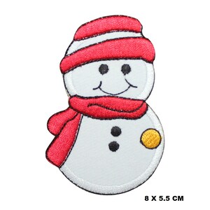 May include: A white snowman with a red hat and scarf. The snowman has a black button nose and two black eyes. The snowman is holding a yellow ball in its right hand. 8 x 5.5 cm