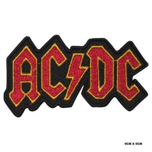 May include: Black and red embroidered iron-on patch with the text "AC/DC" in a bold, stylized font. The patch is 9 cm by 5 cm.