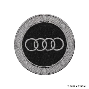 Puede incluir: Un parche bordado en plata y negro con el logotipo de Audi, cuatro anillos entrelazados, sobre un fondo negro. El parche mide 7,5 cm por 7,5 cm.