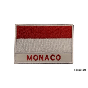 Op de afbeelding: Gestikte patch met de vlag van Monaco. De patch is wit met een rode horizontale streep bovenaan en het woord "MONACO" in rode letters onderaan. De patch meet 9 cm bij 6 cm.