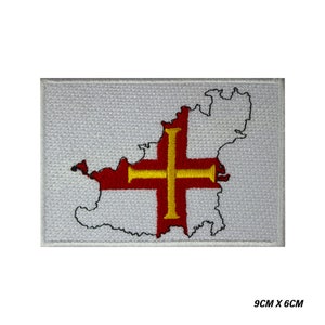 May include: White embroidered patch with a red cross outlined in gold, depicting the outline of the island of Jersey. The patch measures 9 cm by 6 cm.