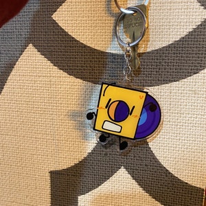 May include: A yellow and purple cartoon character keychain with a record shape. The character has a surprised expression and is holding a record in its hands. The keychain is attached to a silver key ring with a tag that says "Do Not Duplicate".