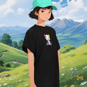 May include: A person wearing a black t-shirt with a colorful cartoon robot graphic, a light blue baseball cap, and grey pants. The person is standing in a field with green grass and pink flowers.