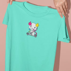 Puede incluir: Una camiseta turquesa con un personaje de dibujos animados impreso en la parte delantera. El personaje es blanco con detalles en rosa, azul y amarillo.