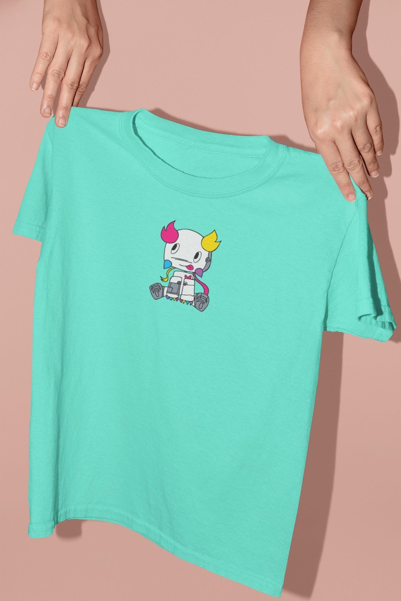 May include: A turquoise t-shirt with a cartoon character printed on the front. The character is white with pink, blue, and yellow accents.