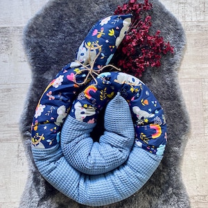 Könnte beinhalten: Ein blaues und weiß gemustertes Baby-Nest mit einem Koala-Design. Das Nest ist zu einem Kreis gerollt und liegt auf einem grauen Kunstfellteppich.