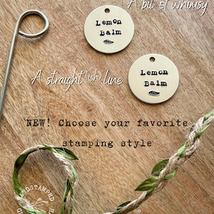 Op de afbeelding: Twee messing labels met de tekst "Lemon Balm" erop gestempeld. De labels liggen op een houten oppervlak met een groen-bruin touw met bladeren. De tekst "A bit of whimsy" en "A straight (ish) line" staat boven de labels. De tekst "NEW! Choose your favourite stamping style" staat onder de labels.