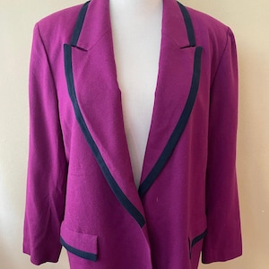 May include: A magenta blazer with black trim on the lapels and pockets. The jacket is displayed on a mannequin. The blazer has a classic design with a notched collar and a two-button closure. The fabric appears to be a wool blend.