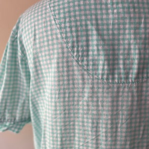May include: A green and white gingham shirt with short sleeves. The shirt has a white collar and a curved seam on the back.