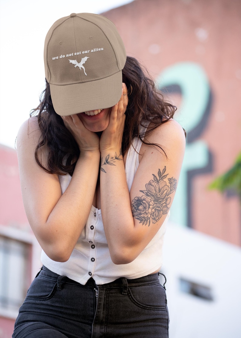 May include: A tan baseball cap with a white embroidered dragon and the text "we do not eat our allies".
