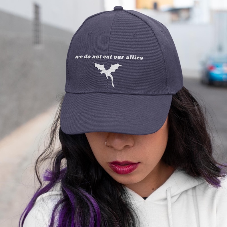 May include: A navy blue baseball cap with a white dragon graphic and the text "we do not eat our allies".