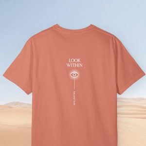 May include: A coral colored t-shirt with a white graphic design on the back. The graphic features an eye with rays of light and the text "LOOK WITHIN" and "Live your truth".