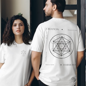 May include: Two white t-shirts with geometric designs. The front of the shirt on the left has a small geometric design with the word "WATER" inside. The back of the shirt on the right has a larger geometric design with the words "CREATION", "HARMONY", "Metatron's Cube", "Divine Proportion", "Platonic Solids", and "Fruit Of Life" around the design.