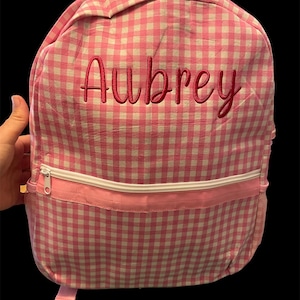 Puede incluir: Mochila de cuadros vichy rosa y blanco con un nombre bordado en rosa "Aubrey" en la parte delantera.