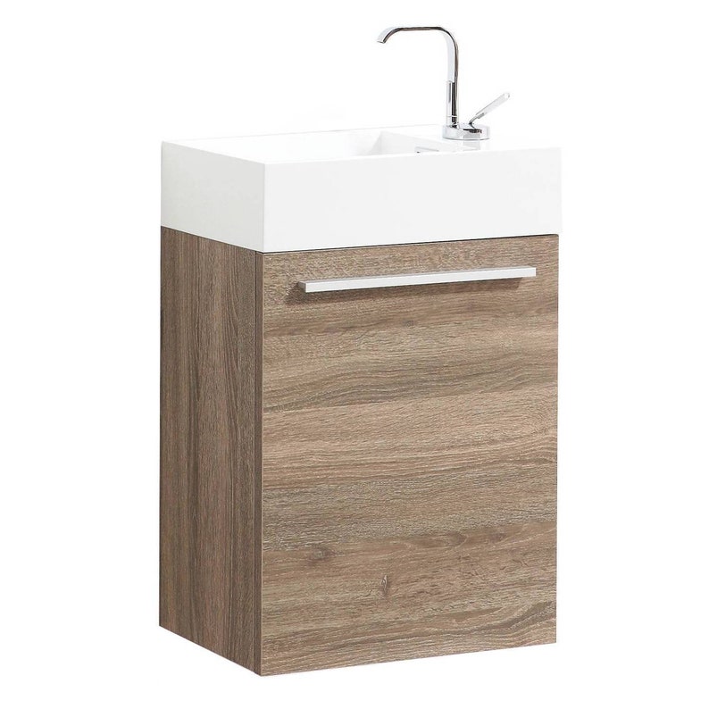 Puede incluir: Un lavabo de cer&aacute;mica blanca con un grifo cromado montado en un mueble de ba&ntilde;o de madera marr&oacute;n con un solo caj&oacute;n. El mueble tiene una manija plateada.