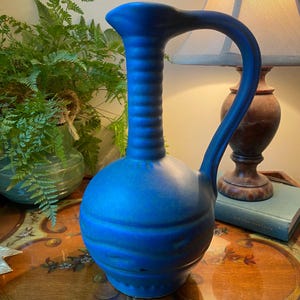 May include: A blue ceramic pitcher with a bulbous body and a tall, slender neck. The pitcher has a textured surface and a handle.