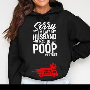 May include: Black hooded sweatshirt with white text that reads "Sorry I'm late my husband had to poop #wifelife". A red graphic of a truck with the words "Ships Fast" is on the front pocket.