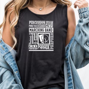 Può includere: Canotta nera con testo bianco. Il testo recita: "PERCUSSION DRILL PRACTICE BRASS HALT MARCHING BAND STRIDE Woodwinds UNIFORM 8 TO 5 FORMATION PARADE PERFORM MUSIC". Include un simbolo della banda musicale.