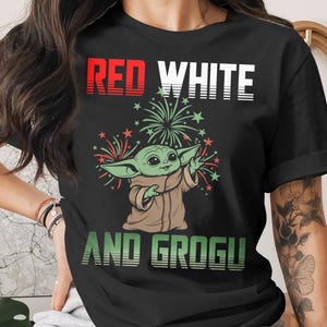 Grogu in a red, white, and patriotic t-shirt with fireworks.