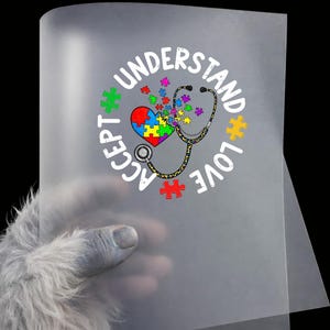 May include: A translucent sheet featuring a design with the words "Understand, Accept, Love" encircling a heart-shaped puzzle and a stethoscope. The heart is composed of puzzle pieces in various colors, with additional puzzle pieces scattered around.