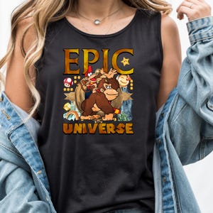 May include: Black tank top featuring a cartoon graphic with the words "EPIC UNIVERSE". The graphic includes a brown gorilla, two monkeys, a star, a mushroom, and a rainbow.
