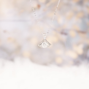 May include: A silver necklace with a delicate pendant featuring a round, clear gemstone set in a fan-shaped design.