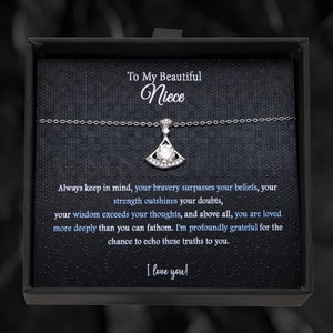 May include: A black gift box with a silver necklace inside. The necklace has a pendant with a clear crystal and a fan-shaped design. The box has a message inside that reads "To My Beautiful Niece. Always keep in mind, your bravery surpasses your beliefs, your strength outshines your doubts, your wisdom exceeds your thoughts, and above all, you are loved more deeply than you can fathom. I'm profoundly grateful for the chance to echo these truths to you. I love you!"