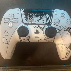 Könnte beinhalten: Weißer PlayStation 5-Controller, der mit einer schwarz-weißen Illustration im Anime-Stil versehen ist. Das Design zeigt ein detailliertes Manga-Gesicht in der Mitte, mit schwarzen Akzenten und Knopffunktionen.