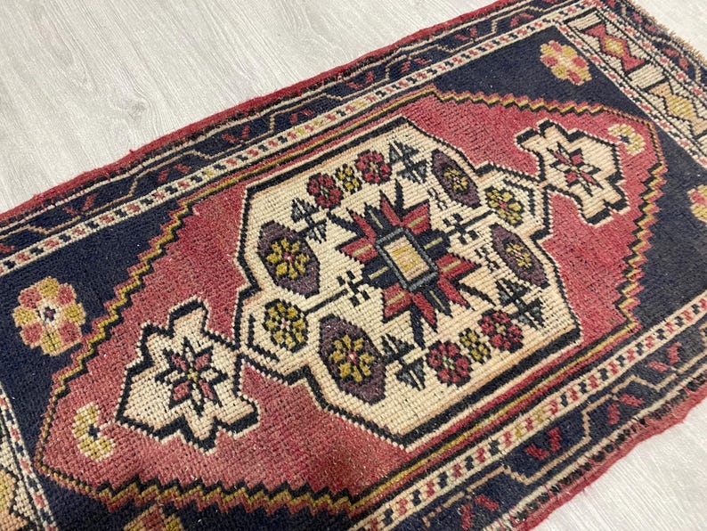 Puede incluir: Una alfombra rectangular que presenta un medall&oacute;n central de color crema con motivos florales geom&eacute;tricos en rojo, amarillo y azul oscuro. La alfombra tiene un borde azul marino y un campo rojo, con complejos patrones tejidos.