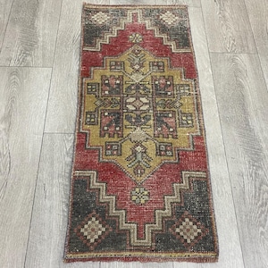May include: A rectangular woven rug featuring a central geometric medallion in shades of mustard yellow, deep red, and charcoal gray. The design includes intricate repeating patterns, small floral motifs, and a stepped border with diamond accents.
