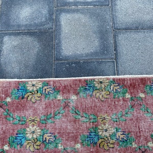 May include: A red rug with a floral pattern in shades of blue, yellow, and green. The rug has a white fringe border.