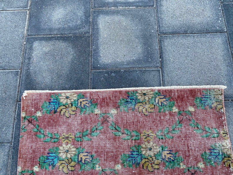 May include: A red rug with a floral pattern in shades of blue, yellow, and green. The rug has a white fringe border.