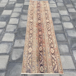 May include: A vintage runner rug with a traditional Persian design. The rug has a beige background with brown, red, and blue floral patterns.