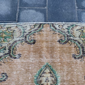 May include: A vintage rug with a beige background and intricate floral patterns in shades of green and black. The rug has a worn and faded look, giving it a rustic and antique feel.