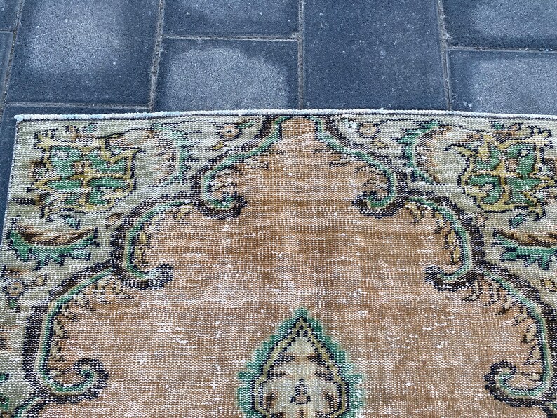 May include: A vintage rug with a beige background and intricate floral patterns in shades of green and black. The rug has a worn and faded look, giving it a rustic and antique feel.