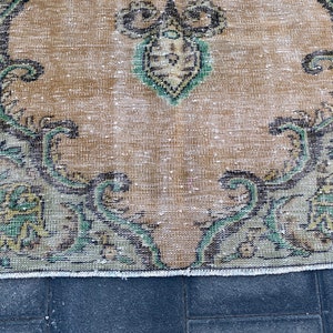 May include: A vintage rug with a faded beige background and a floral pattern in shades of green, black, and gold. The rug has a frayed edge.