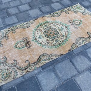 May include: A vintage rug with a beige background and a green and brown floral pattern. The rug has a distressed look and is perfect for adding a touch of bohemian style to your home.