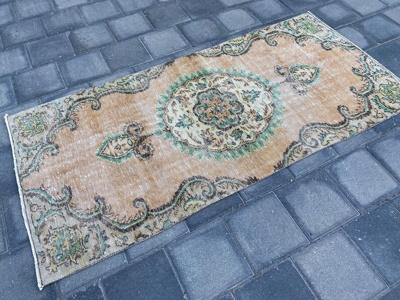May include: A vintage rug with a beige background and a green and brown floral pattern. The rug has a distressed look and is perfect for adding a touch of bohemian style to your home.